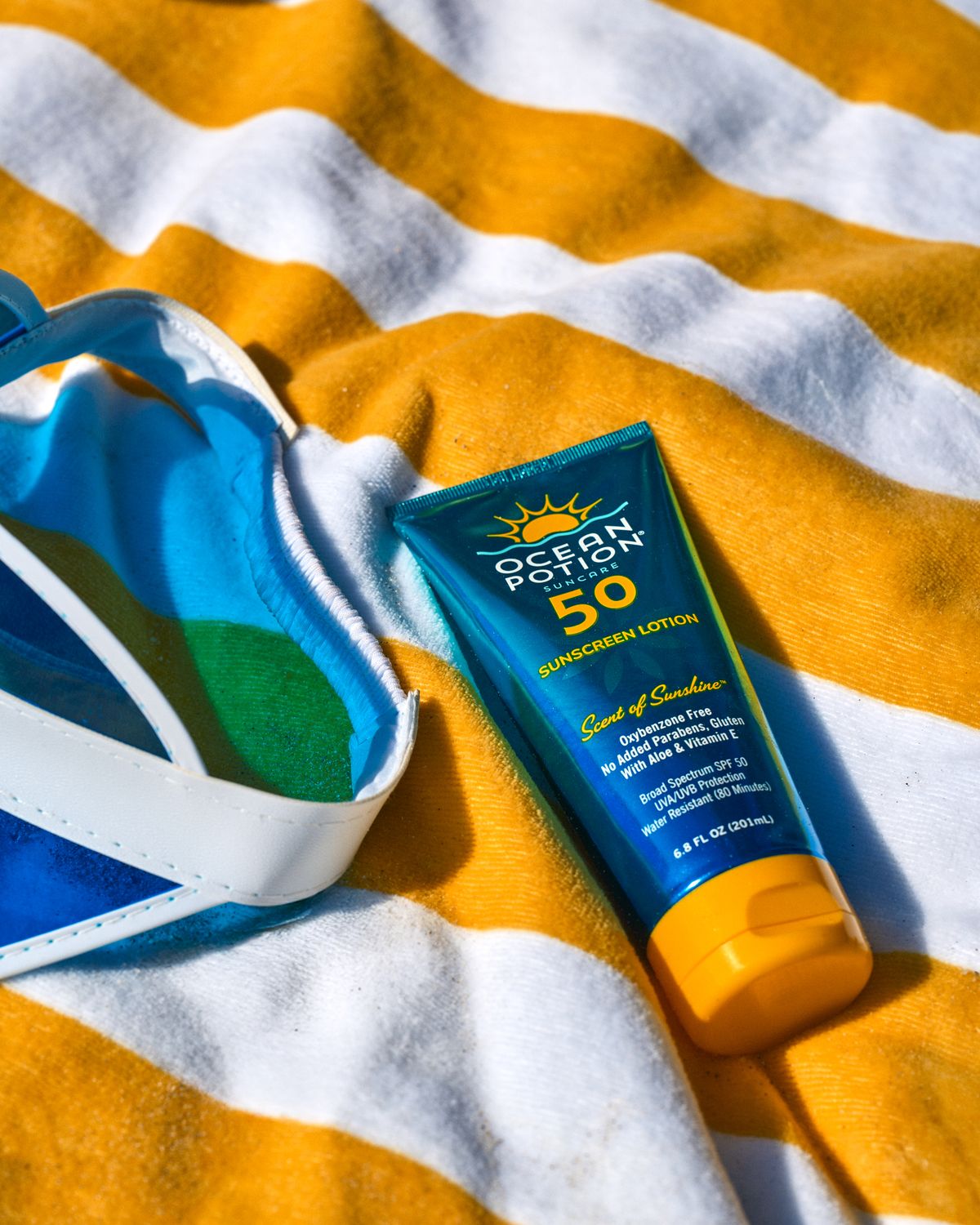 Sunscreen product and blue visor on a striped towel during a commercial swimwear brand shoot in Miami, Florida.