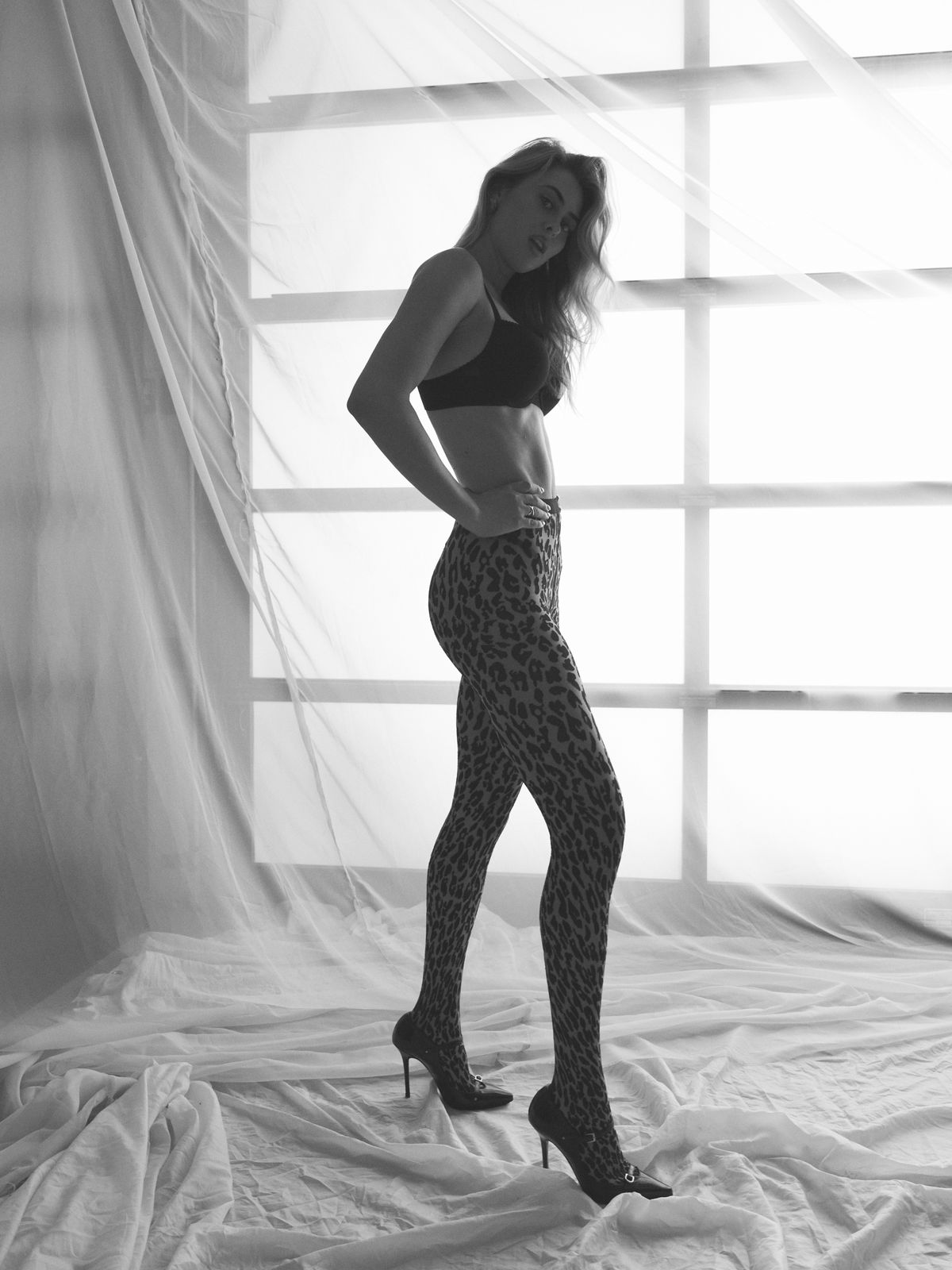 Black-and-white full-length profile of model Julia, hand on hip, leopard-print leggings and heels, gridded studio window, Los Angeles