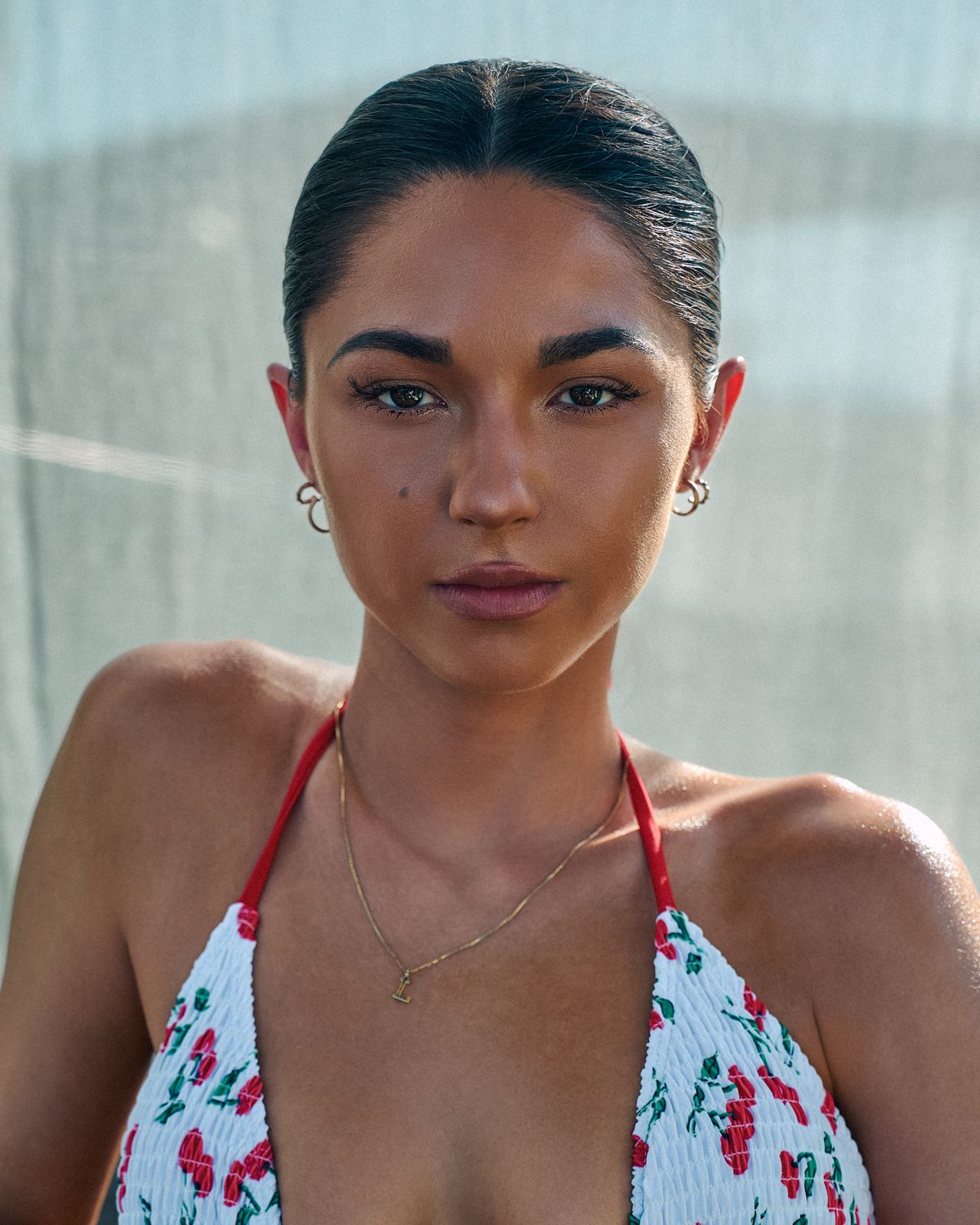 Close beauty portrait of model Lauren in a cherry-print bikini with slicked-back hair and a gold necklace, poolside in Dallas