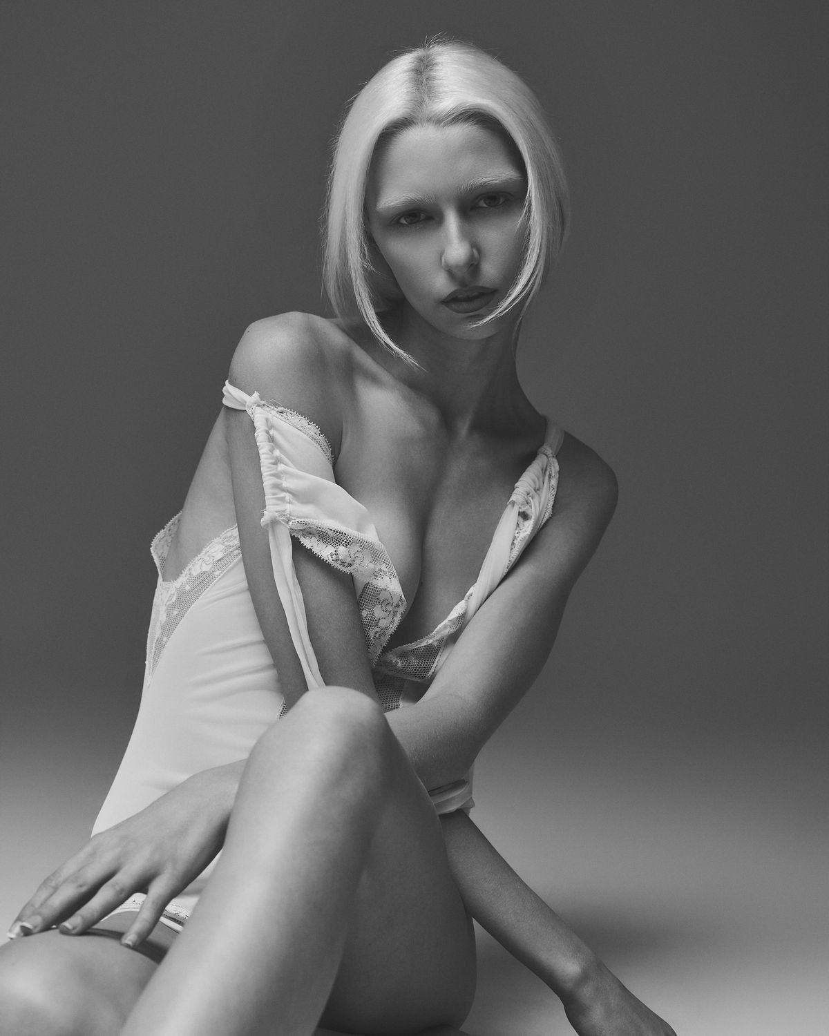 Model Kalie seated in an ivory lace bodysuit slipping off the shoulder, bobbed hair, low-key black-and-white frame, Dallas