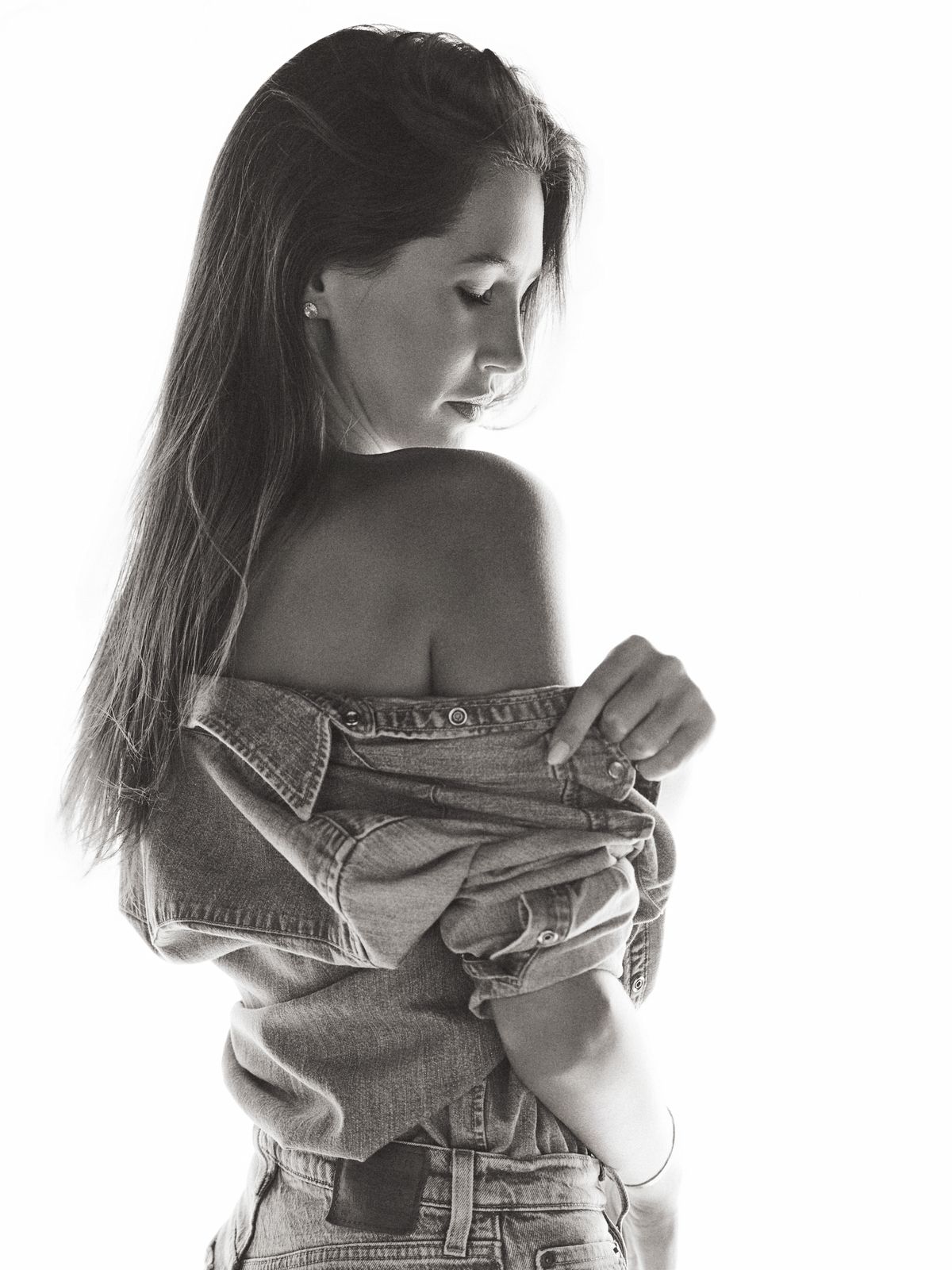 Giovanna from behind with a bare shoulder, holding her denim at the waist, backlit black-and-white frame.