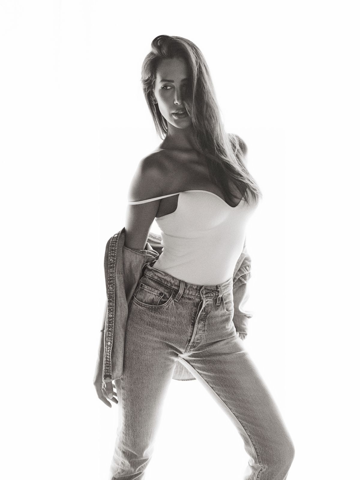 Full-length black-and-white frame of Giovanna in a white top and denim, wide stance against the bright backlight.