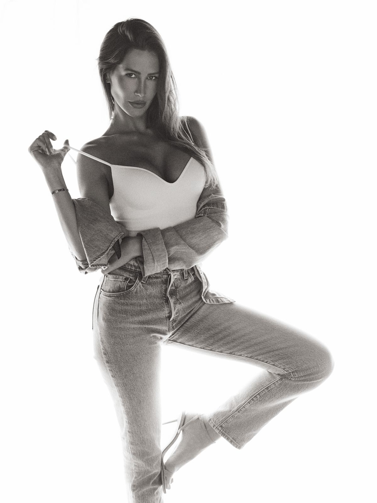 Giovanna leaning back with one foot lifted, easing her top strap, high-key black-and-white frame.