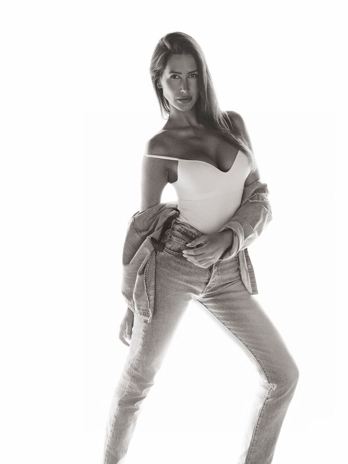 Full-length black-and-white frame of Giovanna in a white off-shoulder top and denim, facing the camera.